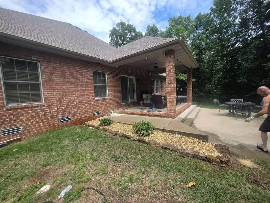Stone-bordered planting bed along a brick house next to a covered patio